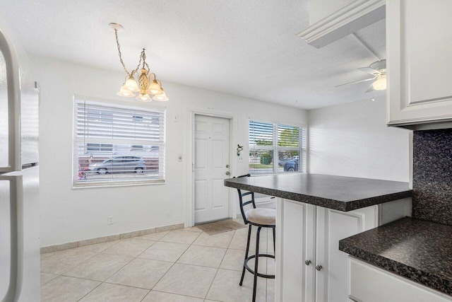 kitchen featuring decorative light fixtures, a breakfast bar area, ceiling fan with notable chandelier, white cabinets, and light tile patterned flooring