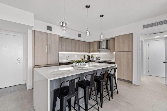 kitchen with a breakfast bar area, hanging light fixtures, light stone countertops, a kitchen island, and wall chimney exhaust hood