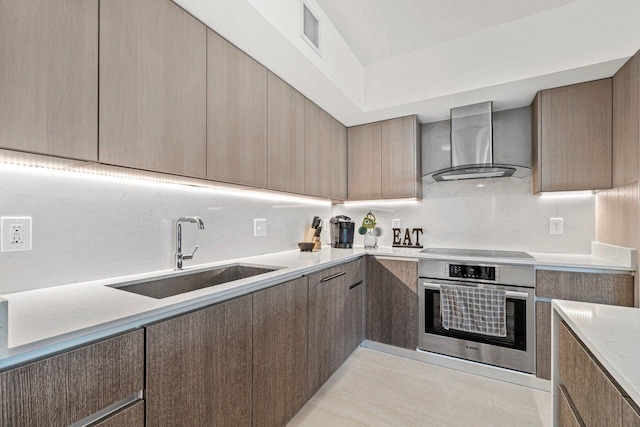 kitchen with wall chimney exhaust hood, modern cabinets, light countertops, stainless steel oven, and a sink