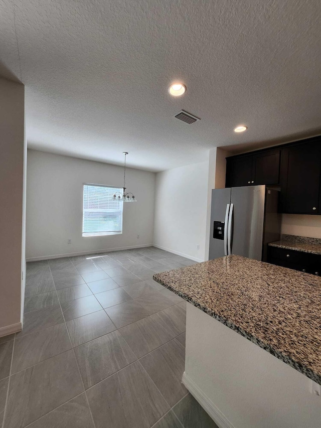 kitchen with light tile patterned flooring, light stone counters, hanging light fixtures, a textured ceiling, and stainless steel fridge