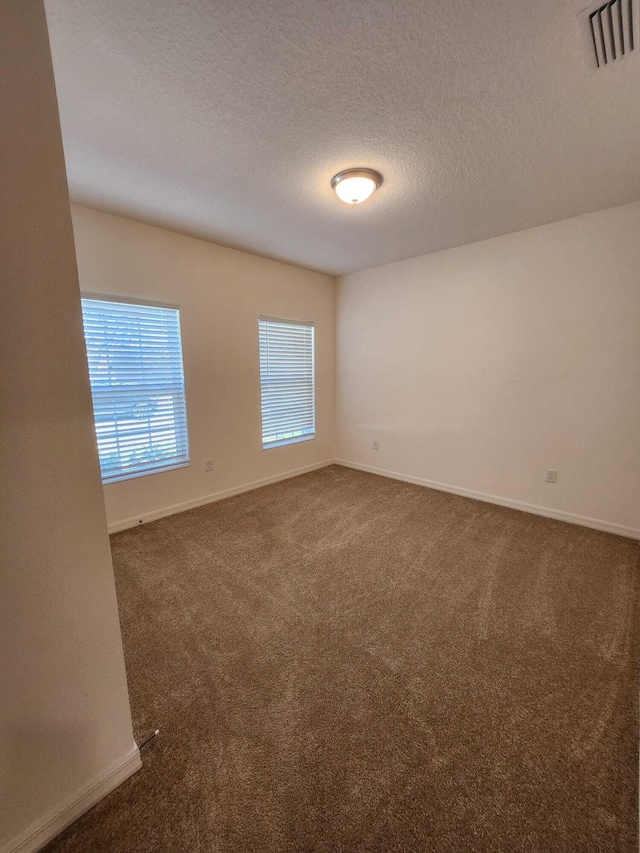 unfurnished room featuring plenty of natural light, a textured ceiling, and dark carpet