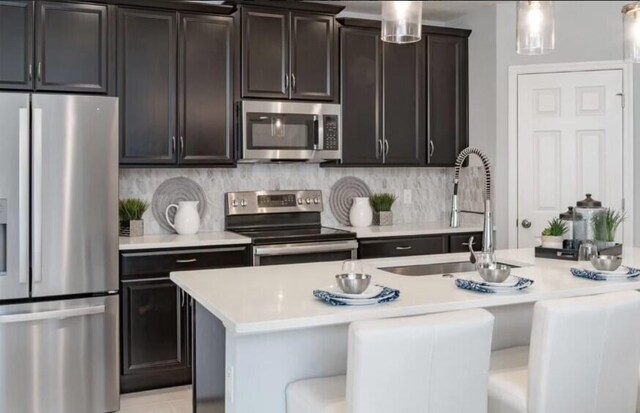 kitchen with light stone countertops, appliances with stainless steel finishes, ceiling fan, a breakfast bar area, and an island with sink