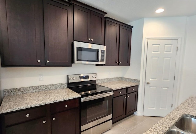 kitchen with light tile patterned flooring, appliances with stainless steel finishes, dark brown cabinets, and light stone counters