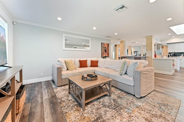 living room with crown molding, a skylight, and light hardwood / wood-style floors