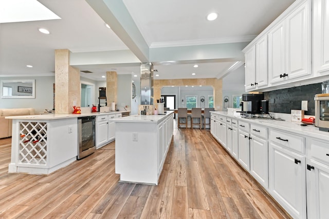 kitchen featuring crown molding, white cabinetry, a center island, wine cooler, and kitchen peninsula