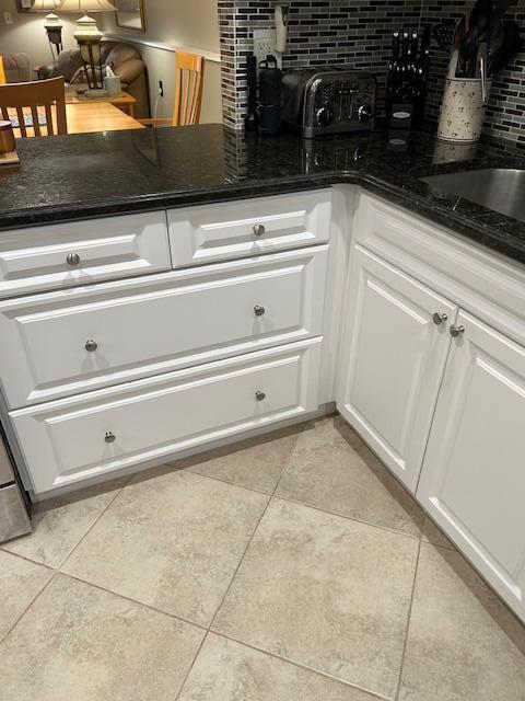 kitchen with light tile patterned floors, white cabinets, dark stone counters, and decorative backsplash