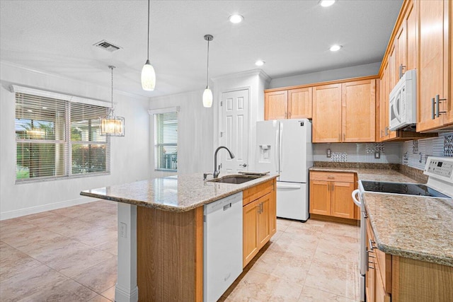 kitchen with light stone countertops, sink, hanging light fixtures, white appliances, and a center island with sink