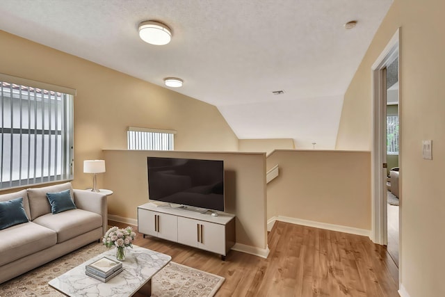 living room featuring a textured ceiling, light hardwood / wood-style flooring, and lofted ceiling