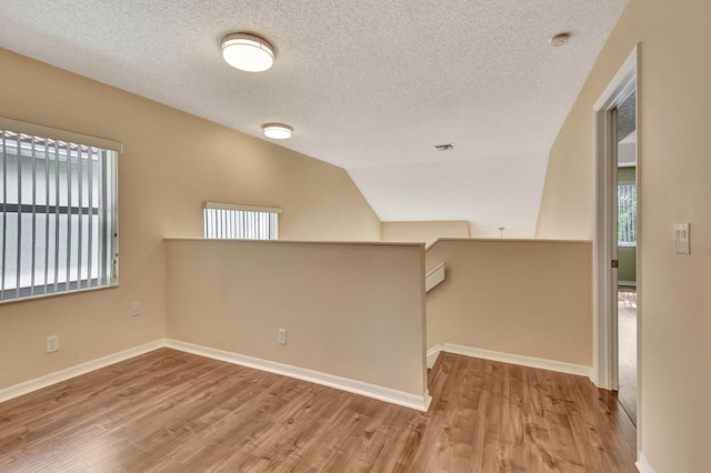 empty room with a textured ceiling, light hardwood / wood-style floors, and lofted ceiling