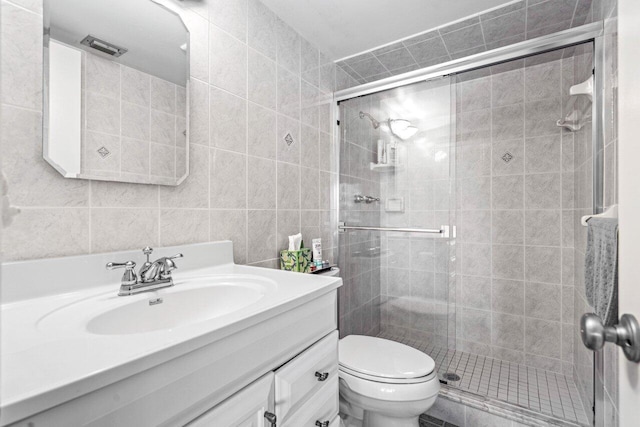 bathroom featuring a shower with door, vanity, tile walls, and toilet