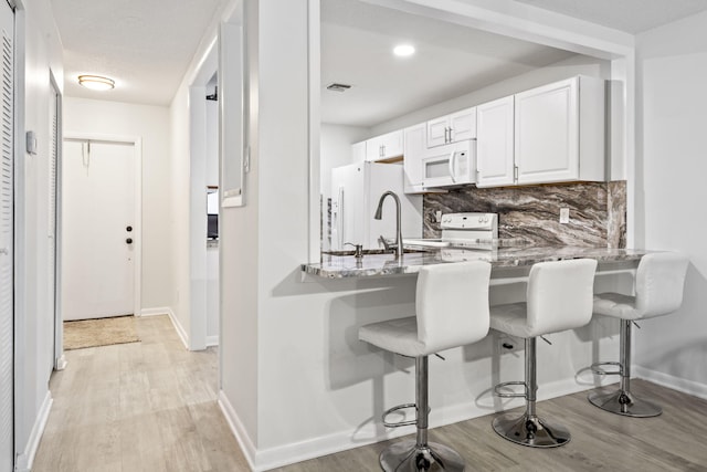 kitchen with white appliances, kitchen peninsula, light stone countertops, white cabinets, and tasteful backsplash