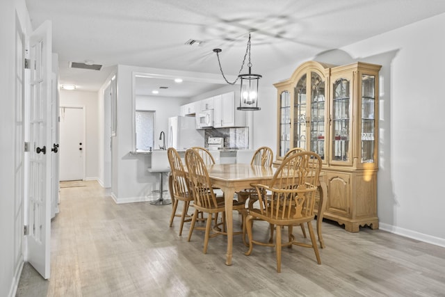 dining area with sink, light wood-type flooring, and a chandelier