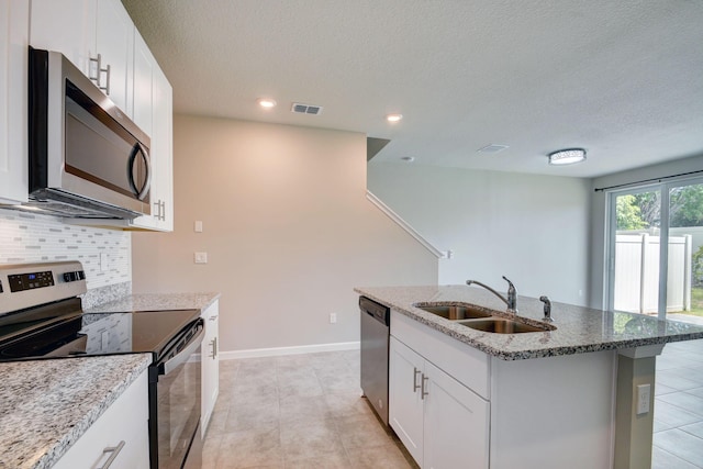 kitchen with white cabinets, sink, light stone countertops, an island with sink, and appliances with stainless steel finishes