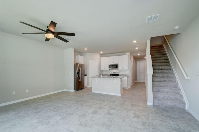 kitchen featuring white cabinetry, ceiling fan, stainless steel appliances, backsplash, and a center island with sink