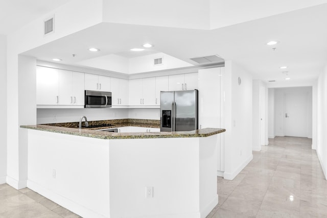 kitchen featuring white cabinets, kitchen peninsula, appliances with stainless steel finishes, and dark stone counters