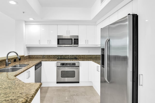 kitchen featuring appliances with stainless steel finishes, dark stone countertops, white cabinets, and sink