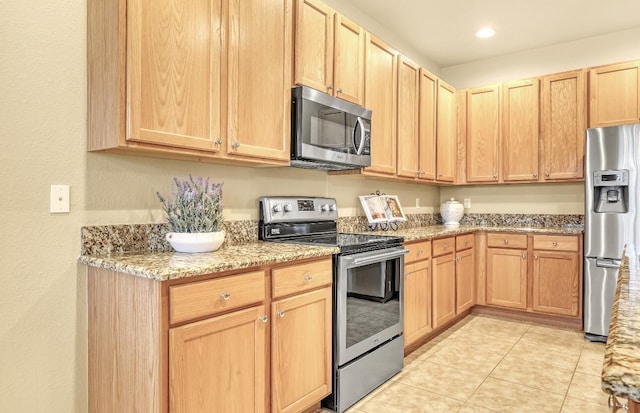 kitchen with light tile patterned floors, light brown cabinetry, light stone counters, and stainless steel appliances