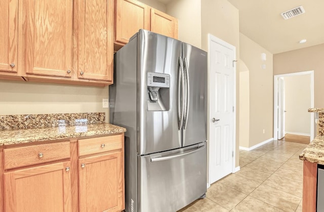 kitchen featuring stainless steel refrigerator with ice dispenser, light tile patterned flooring, and light stone countertops