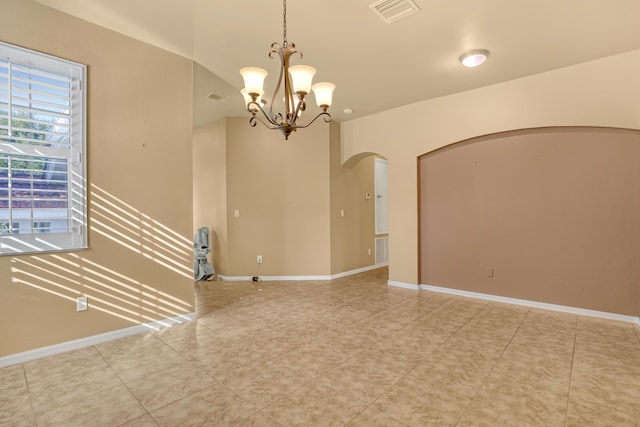 tiled spare room featuring a chandelier