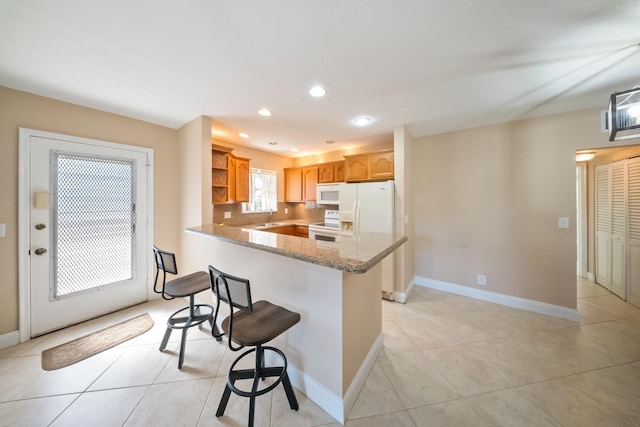 kitchen featuring light stone counters, kitchen peninsula, white appliances, a kitchen bar, and light tile patterned floors