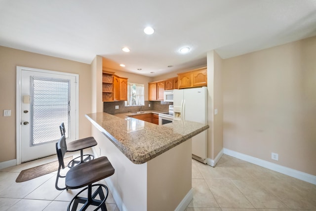 kitchen featuring sink, light stone counters, kitchen peninsula, white appliances, and a kitchen bar