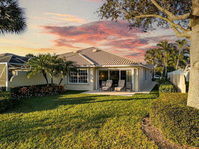 back house at dusk featuring a patio and a lawn