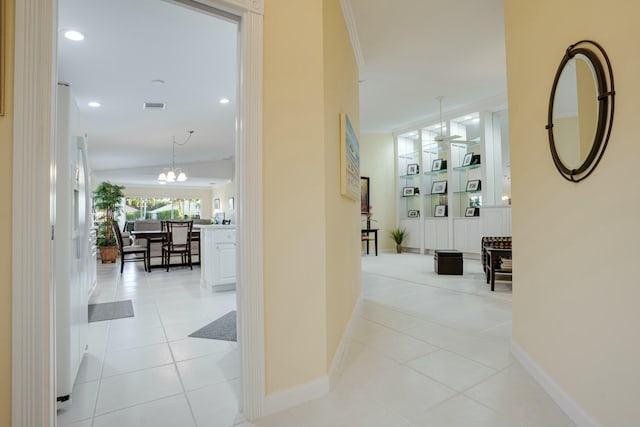 hallway featuring crown molding, built in features, light tile patterned floors, and a chandelier