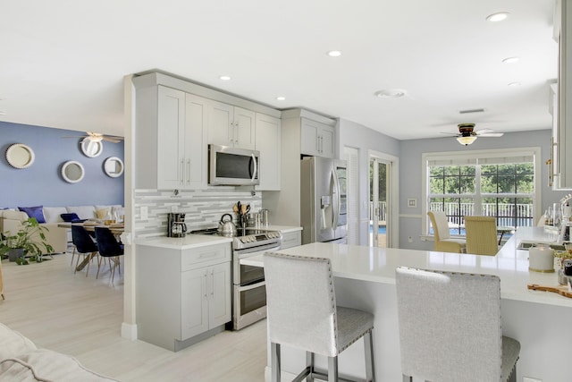 kitchen with kitchen peninsula, a kitchen breakfast bar, tasteful backsplash, stainless steel appliances, and ceiling fan