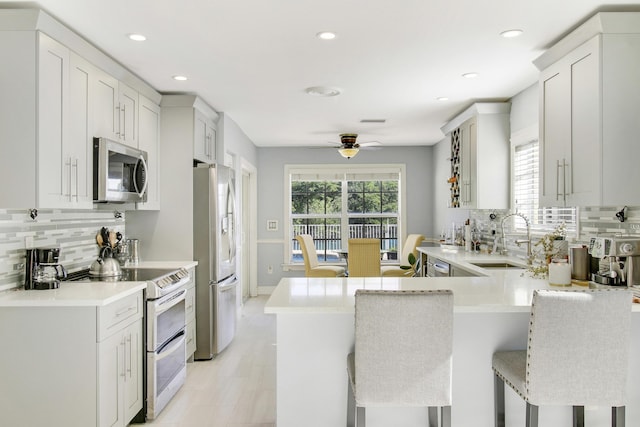 kitchen featuring kitchen peninsula, a kitchen breakfast bar, stainless steel appliances, ceiling fan, and white cabinetry