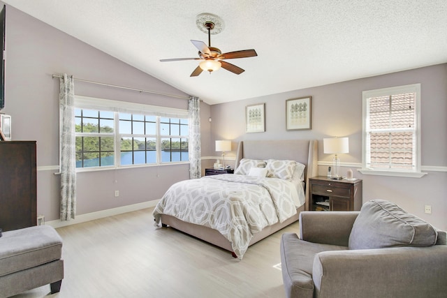 bedroom with light wood-type flooring, a textured ceiling, vaulted ceiling, ceiling fan, and a water view