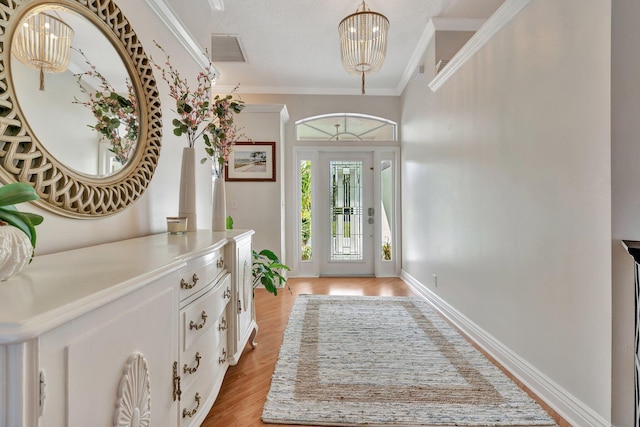 foyer entrance with an inviting chandelier, light hardwood / wood-style floors, and crown molding