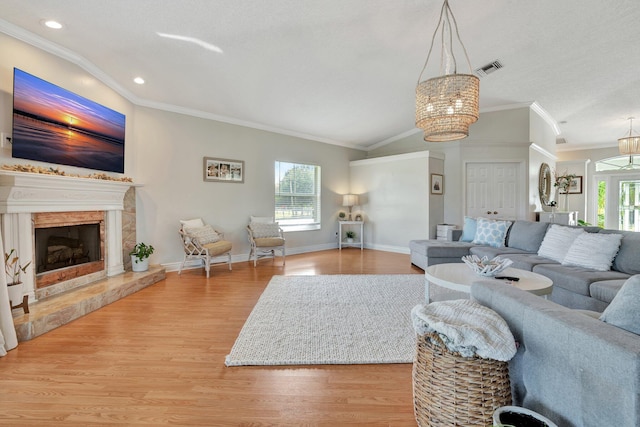 living room with vaulted ceiling, light hardwood / wood-style floors, a notable chandelier, ornamental molding, and a fireplace