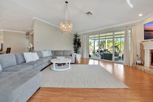 living room featuring a notable chandelier, light wood-type flooring, crown molding, and a fireplace