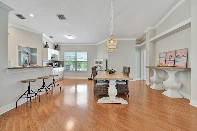 dining area with light wood-type flooring, a textured ceiling, and ornamental molding