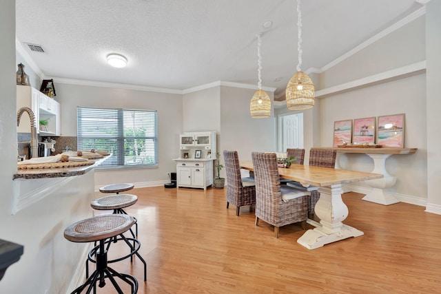 dining space featuring a textured ceiling, light hardwood / wood-style floors, crown molding, and sink