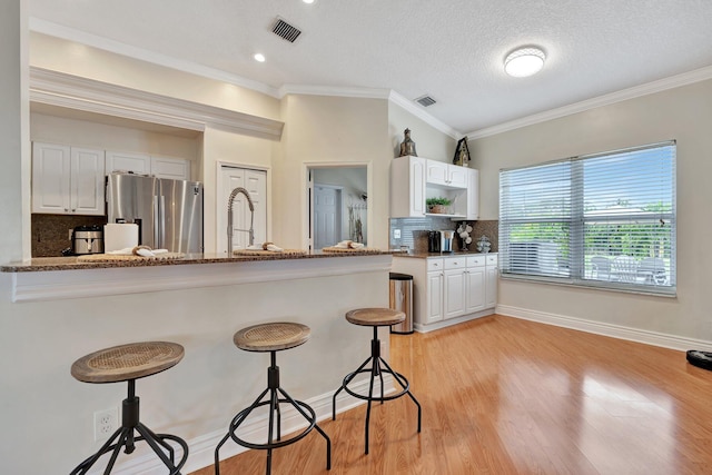 kitchen with white cabinets, tasteful backsplash, kitchen peninsula, and stainless steel refrigerator with ice dispenser