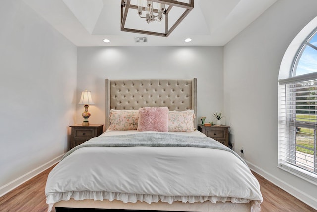 bedroom featuring a raised ceiling, an inviting chandelier, multiple windows, and light hardwood / wood-style floors