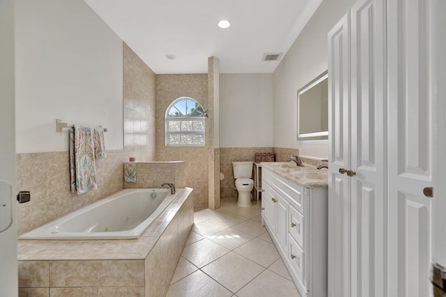 bathroom with toilet, tiled bath, tile walls, tile patterned floors, and vanity