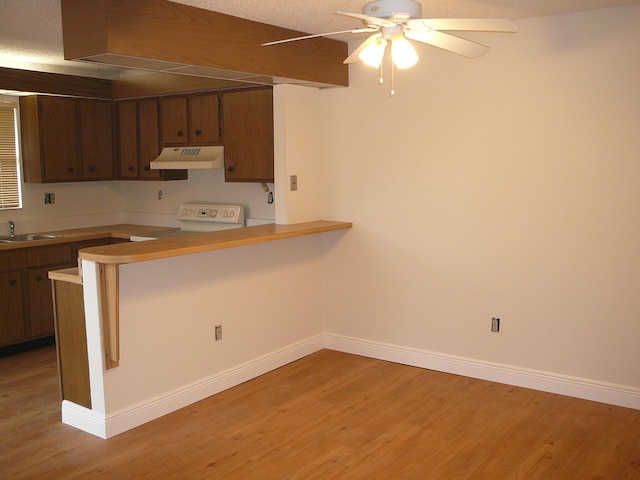 kitchen featuring kitchen peninsula, stove, light wood-type flooring, a textured ceiling, and sink