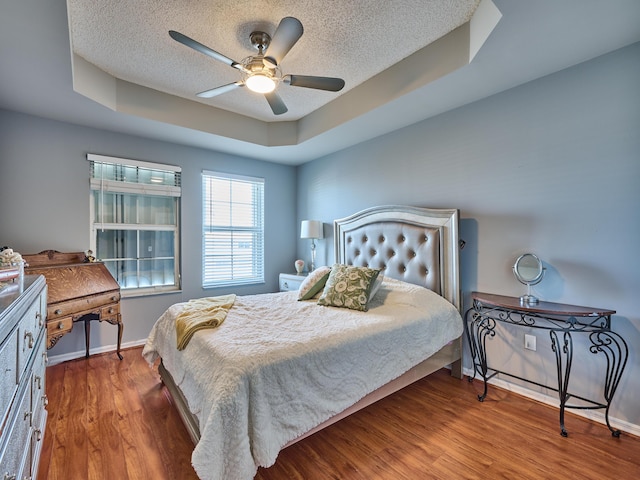 bedroom featuring a raised ceiling, ceiling fan, a textured ceiling, and hardwood / wood-style flooring