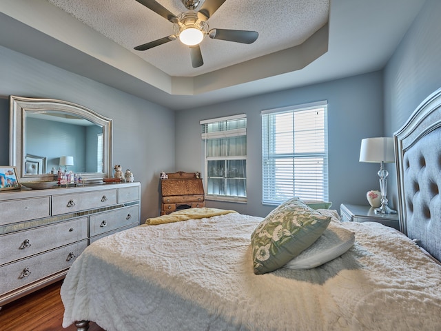 bedroom featuring wood-type flooring, a textured ceiling, a tray ceiling, and ceiling fan