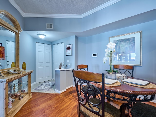 dining space with a textured ceiling, wood-type flooring, and crown molding