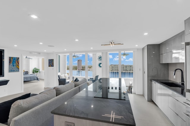 kitchen with floor to ceiling windows, dark stone counters, sink, a water view, and gray cabinets