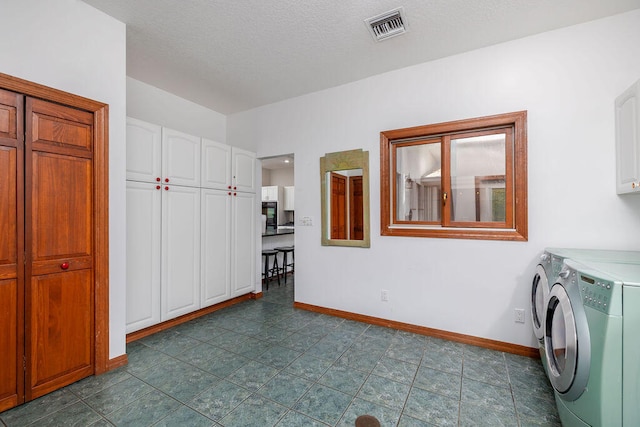 clothes washing area with cabinets, a textured ceiling, and washing machine and dryer