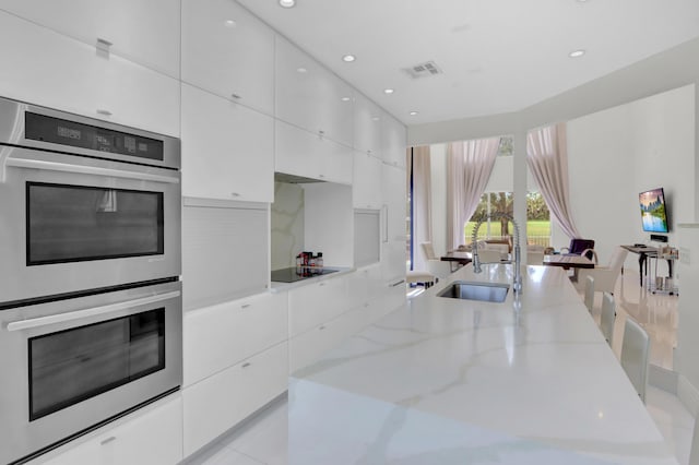 kitchen featuring light stone counters, black electric cooktop, double oven, sink, and white cabinets