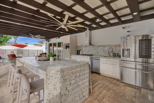 kitchen featuring decorative backsplash, stainless steel appliances, sink, wall chimney range hood, and white cabinetry