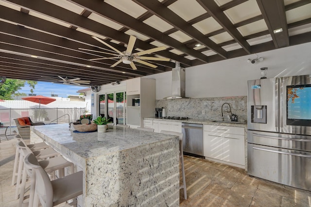 kitchen with light stone countertops, wall chimney range hood, backsplash, white cabinets, and appliances with stainless steel finishes