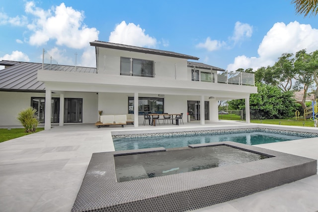 rear view of house with a pool with hot tub, outdoor lounge area, a balcony, and a patio