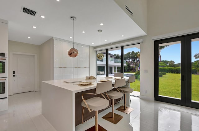 kitchen featuring french doors, a kitchen breakfast bar, light tile patterned floors, decorative light fixtures, and white cabinetry