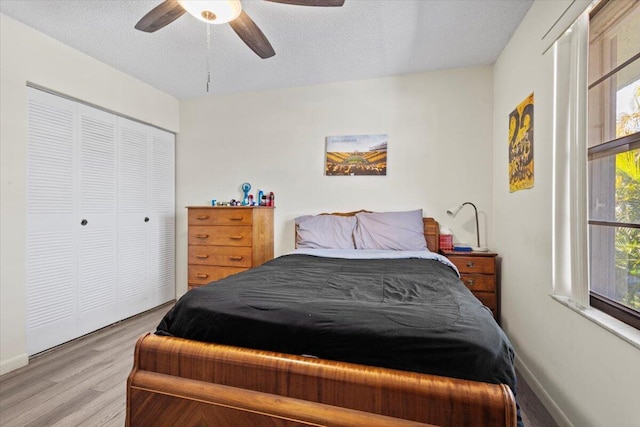 bedroom with a textured ceiling, a closet, light hardwood / wood-style flooring, and ceiling fan